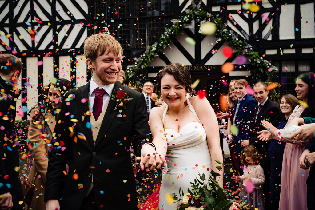 A couple holding hands being showered in colourful confetti