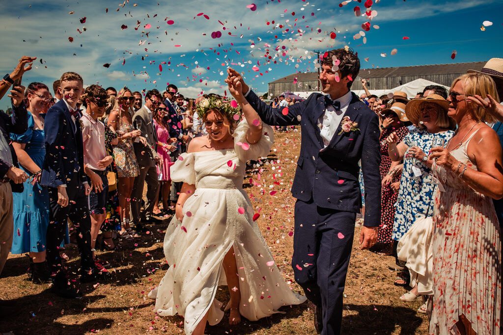 A couple walking through a field, with confetti thrown by their guests.