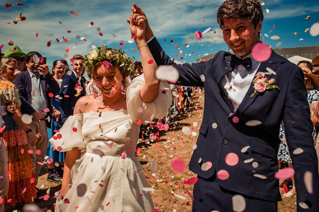 A couple walking through a field, with confetti thrown by their guests.