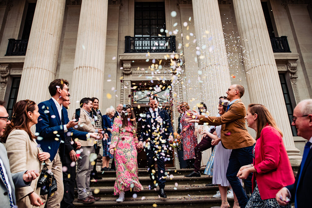 A couple walking through a field, with confetti thrown by their guests at Old Marylebone Town Hall.