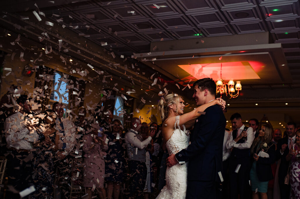 A happy couple dancing their first dance. Their guest are setting off confetti cannons.