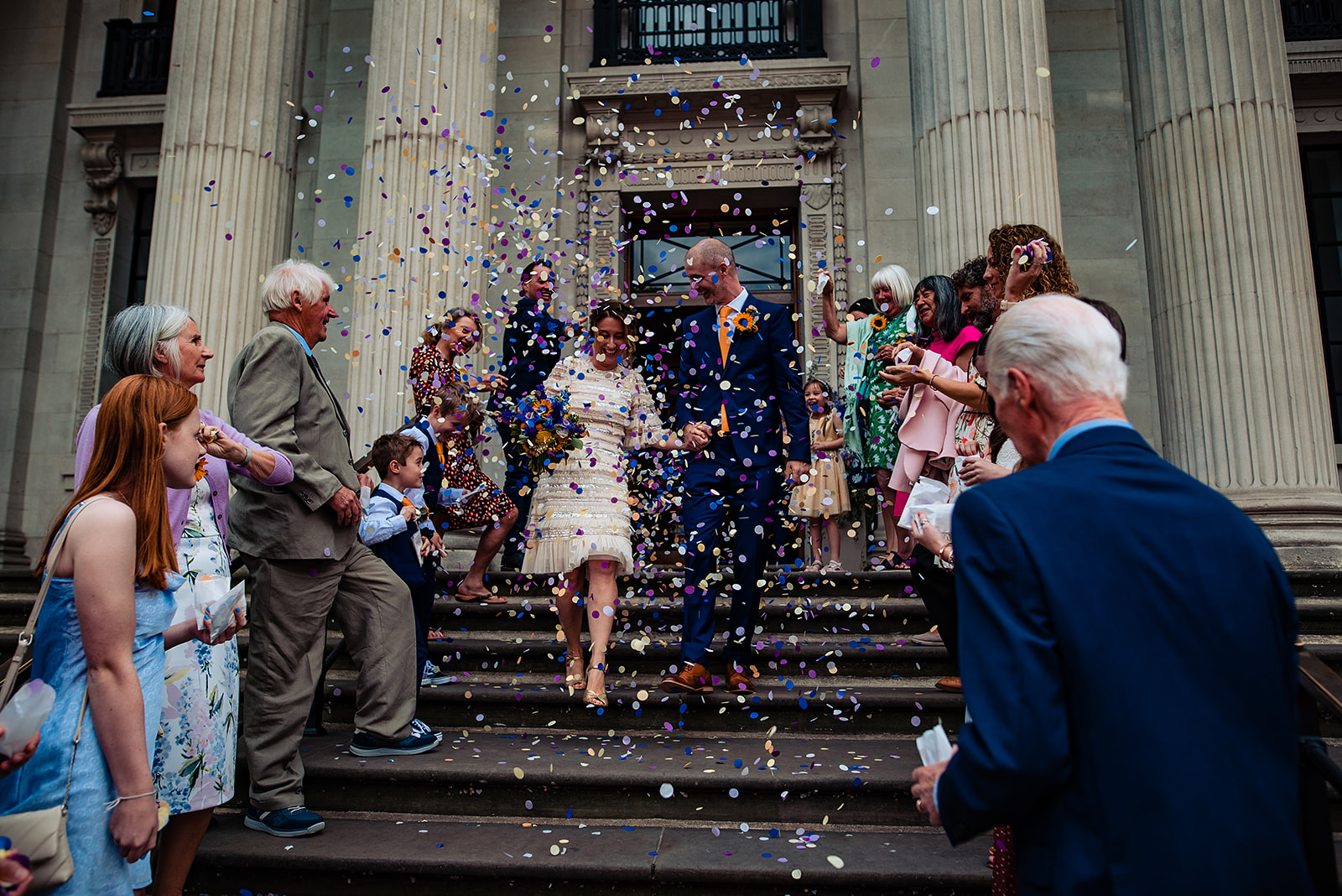 A couple walking down the Old Marylebone Town Hall. With Flutter Darlings confetti being thrown in the air. 