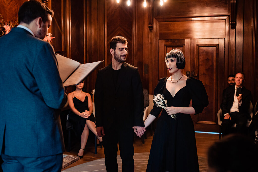 A wedding ceremony in Marylebone Town Hall, London. The bride and groom both wear black. 