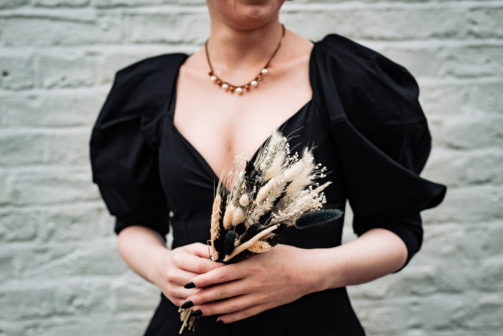 A bride holds a dried flower bridal bouquet, wearing a black Khaite wedding dress and a necklace.