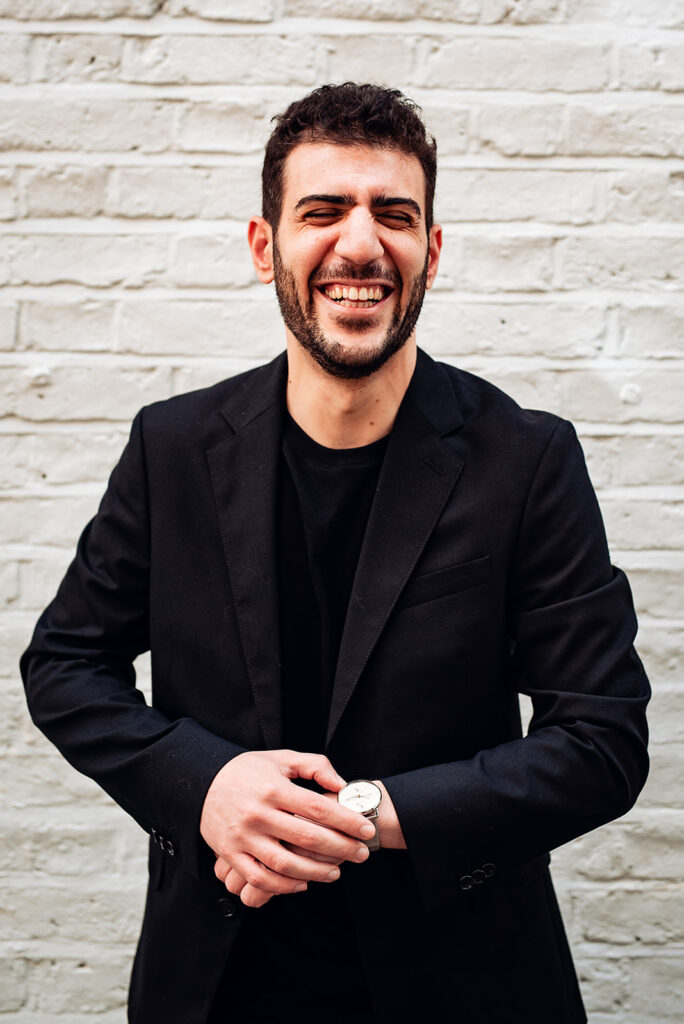 A groom laughs - he is wearing a casual black t shirt with a black jacket. 