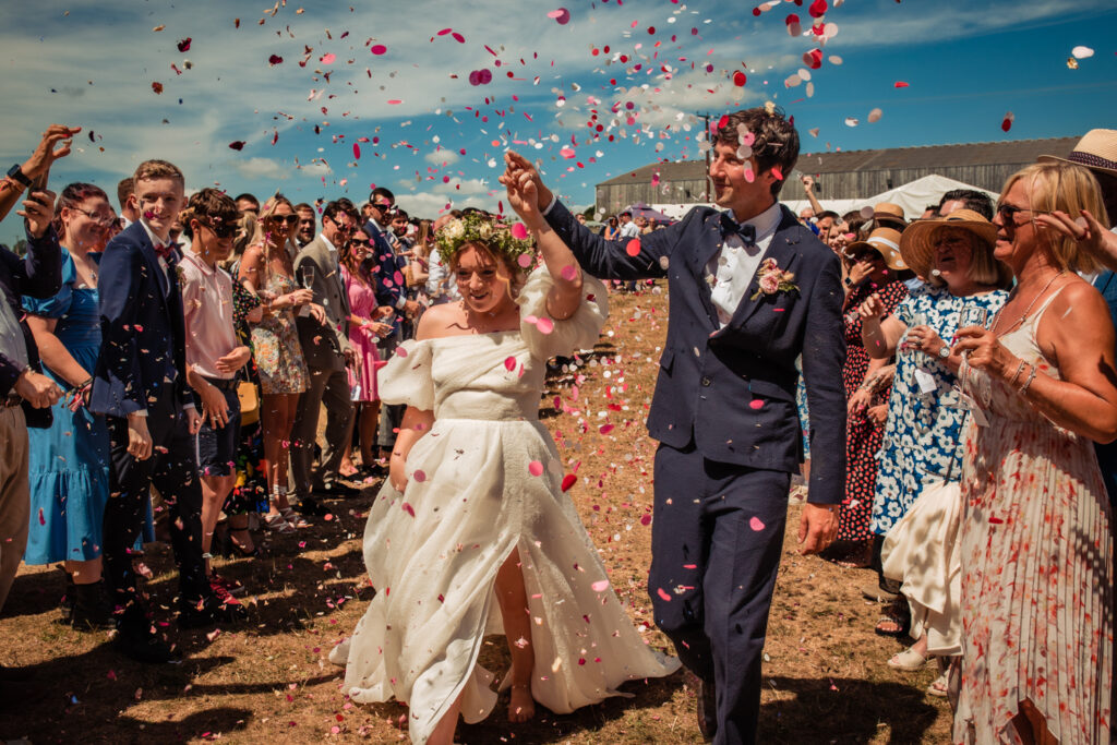 A bride and groom on a beach walk through a showering of confetti, thrown by the guests.