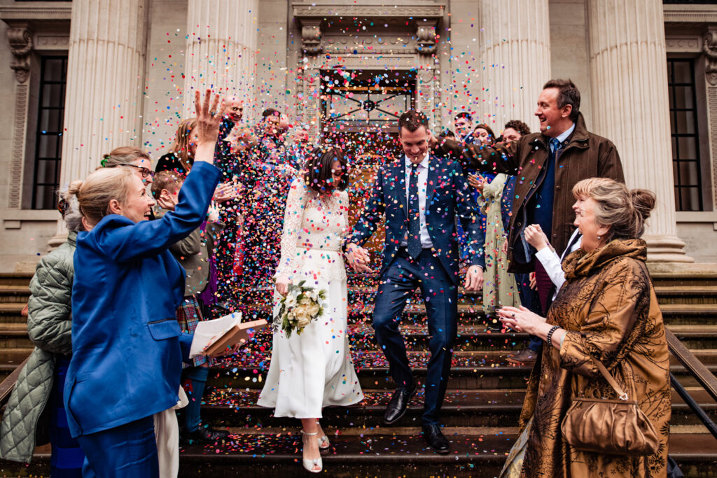 A bride and groom walk through a showering of confetti, thrown by the guests.