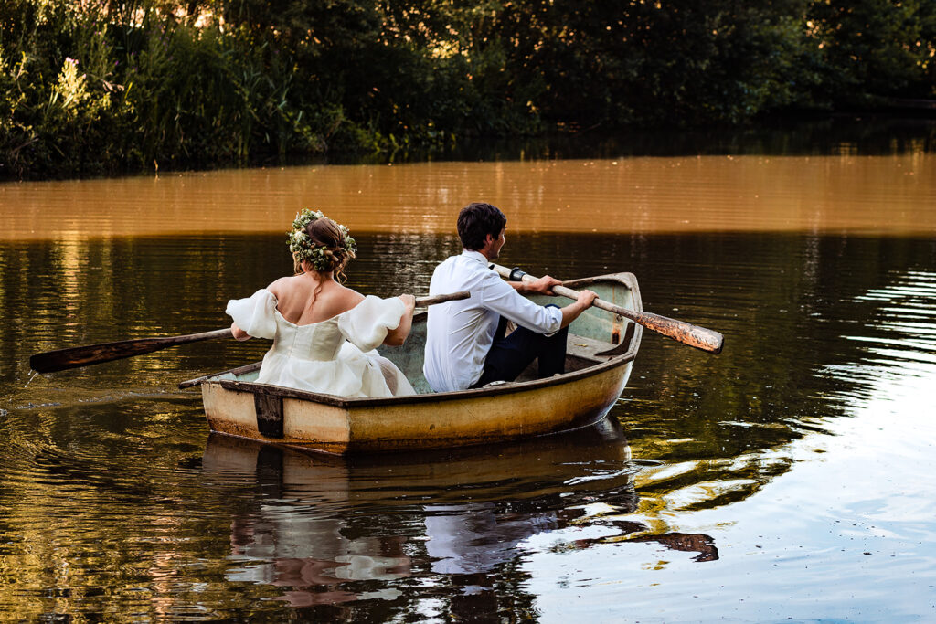 a bride and groom row in a small boat together on a lake.