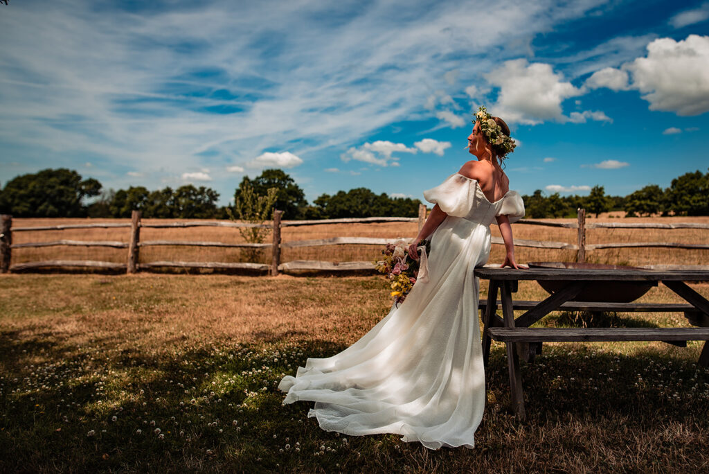 A gorgeous summer days, bride is sitting on a picnic bench looking out towards the sky.