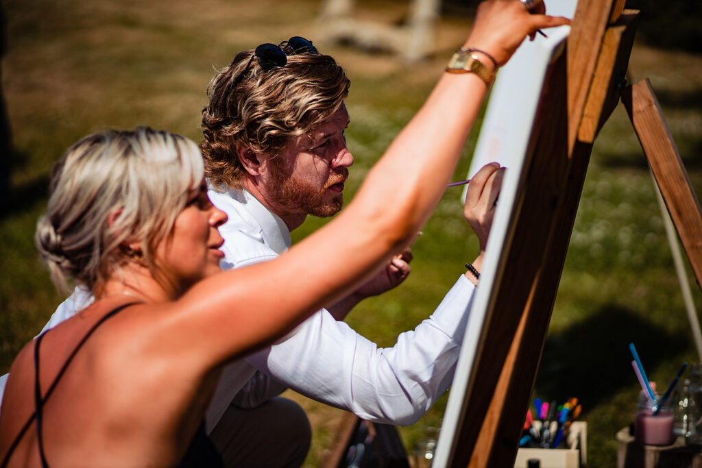Wedding guests add artwork to a blank canvas at a festival style wedding