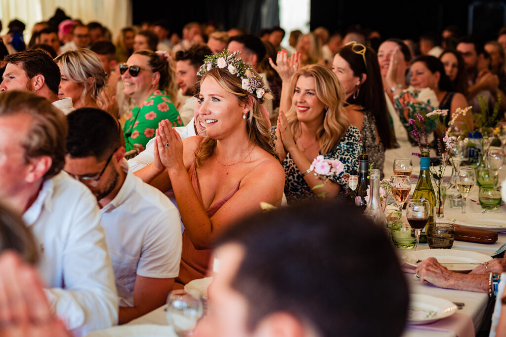 A summer festival wedding at Frickley Lake: Wedding guests applaud a speech at a summery festival wedding 