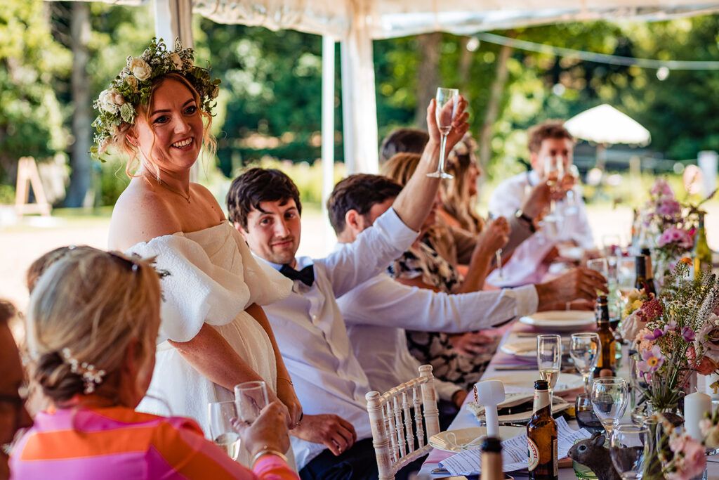 guests raise a toast as a bride stands to give a speech at her wedding reception