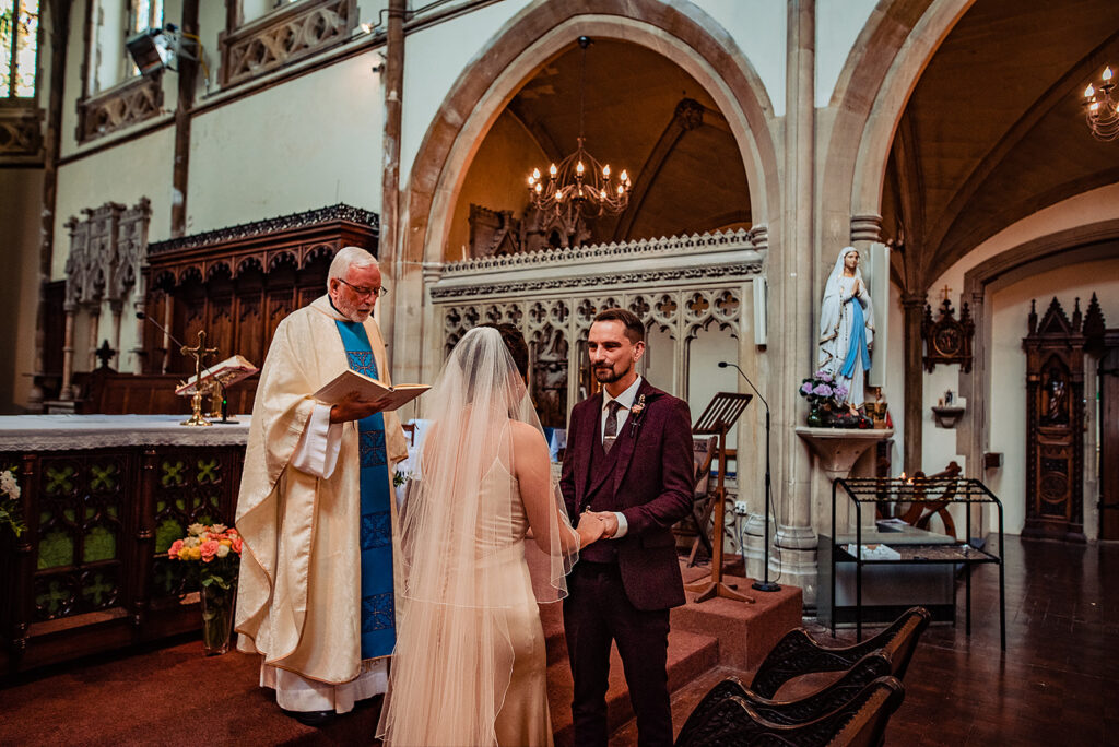 The bride and groom exchange vows at their Catholic wedding ceremony in front of the priest. 