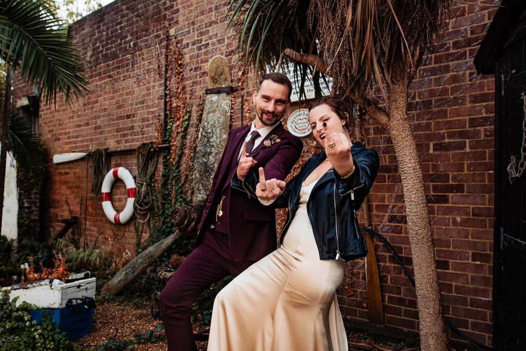 Details from a couple's shoot with a bride and groom after their wedding ceremony. The bride wears a leather jacket and embroidered trainers in a goth chick vibe. They both stick their ring fingers up at the camera.