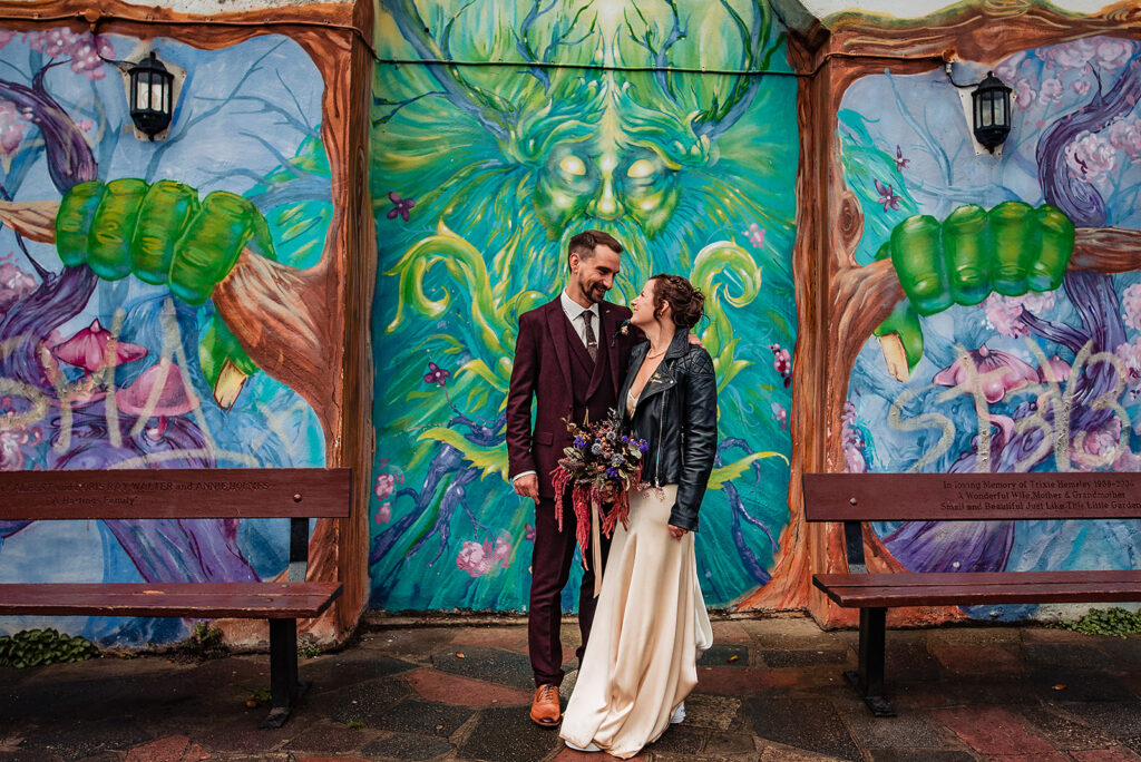 An Alternative wedding: the bride  (wearing a leather jacket) and groom at a goth chick wedding in front of some urban artwork. 

