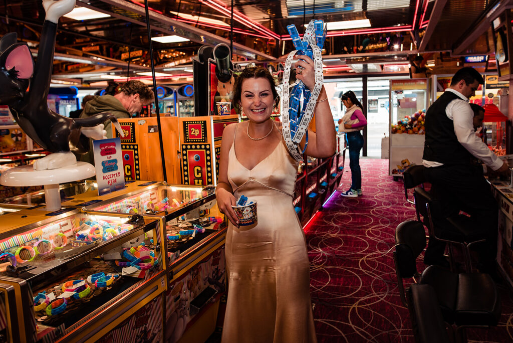 An Alternative wedding: A bride and groom rent a gaming casino by the coast for their entertainment. All the guests celebrate by playing arcade games. The bride holds her tickets and laughs. 
