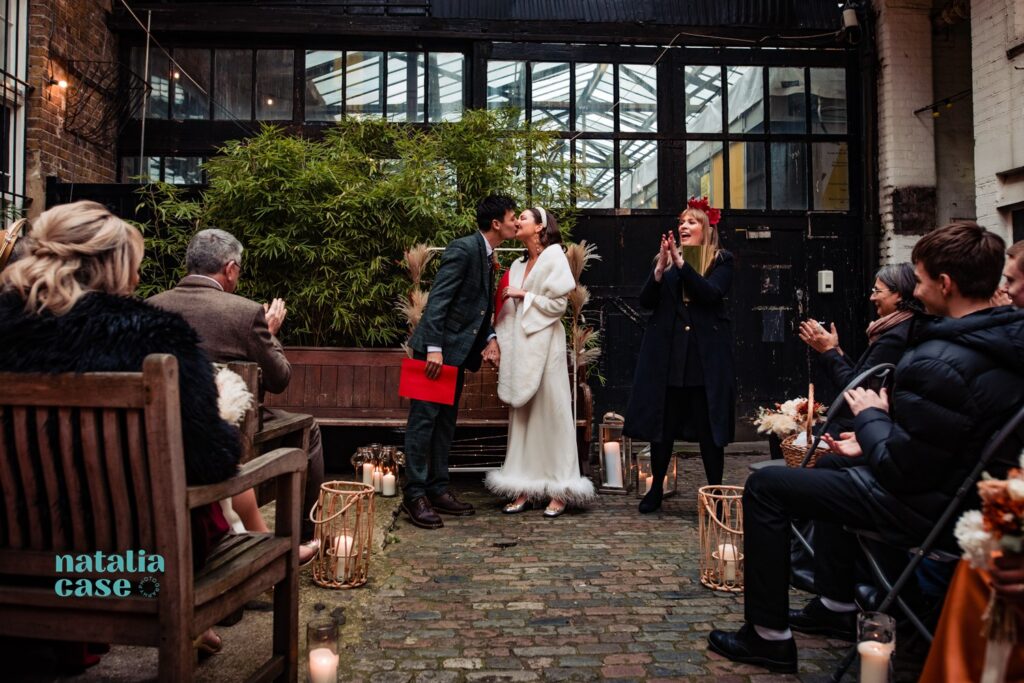 A bride and groom laugh and embrace at the end of their winter wedding ceremony at The Depot N7, London. 