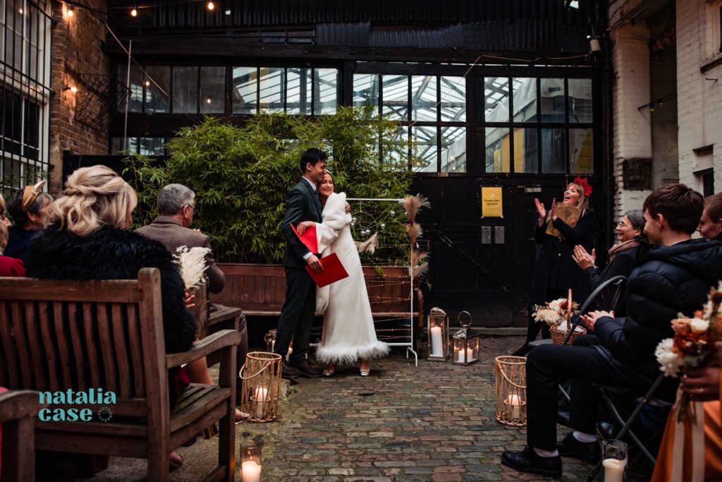 A bride and groom laugh and embrace at the end of their winter wedding ceremony at The Depot N7, London. 