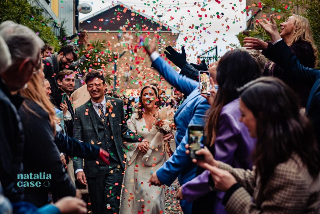 A bride and groom laugh and smile as they walk through a shower of confetti at the end of their winter wedding ceremony. 