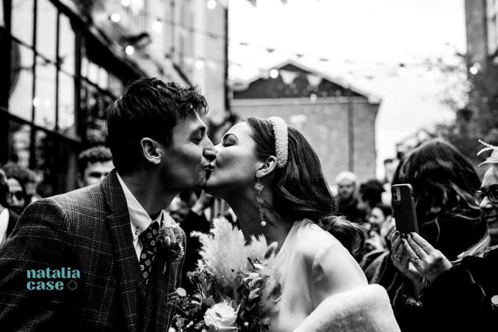 A bride and groom kiss as they walk through a shower of confetti at the end of their winter wedding ceremony. 