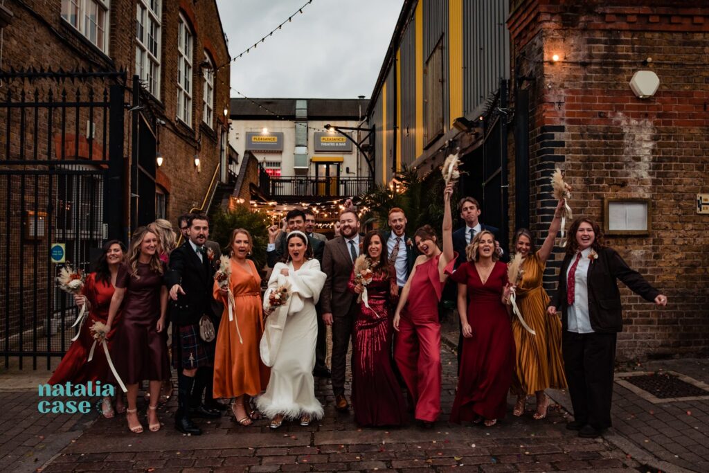The bridal party pose for a group photo. The bridesmaids wear dresses in autumnal colours. 