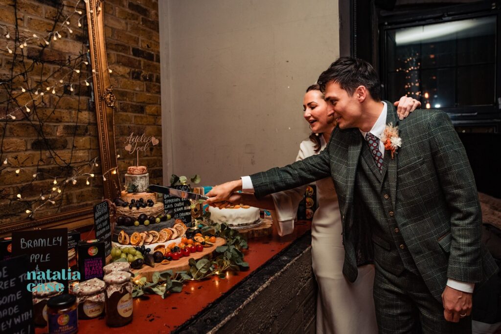 The bride and groom cut their wedding cake, which is actually made of different types of cheese. 
