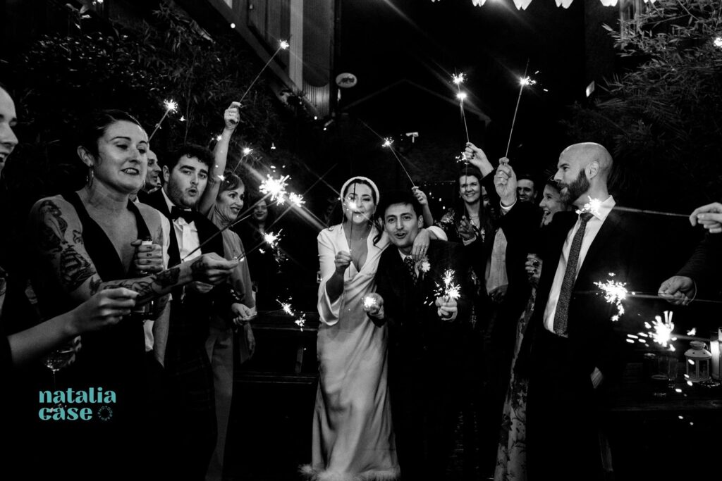 A bride and groom walk through and aisle of sparklers held by their guests, at the evening reception at their winter wedding. 