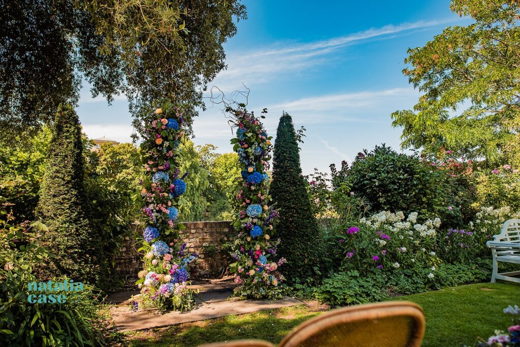 Wedding florals by Flora and Bee - an arch of beautiful flowers in bright summer colours, blues and pinks with dahlias