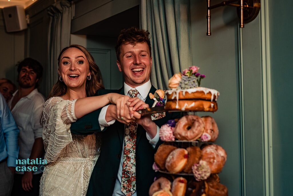 Bride and groom cut their wedding cake, while is actually a tower of donuts.