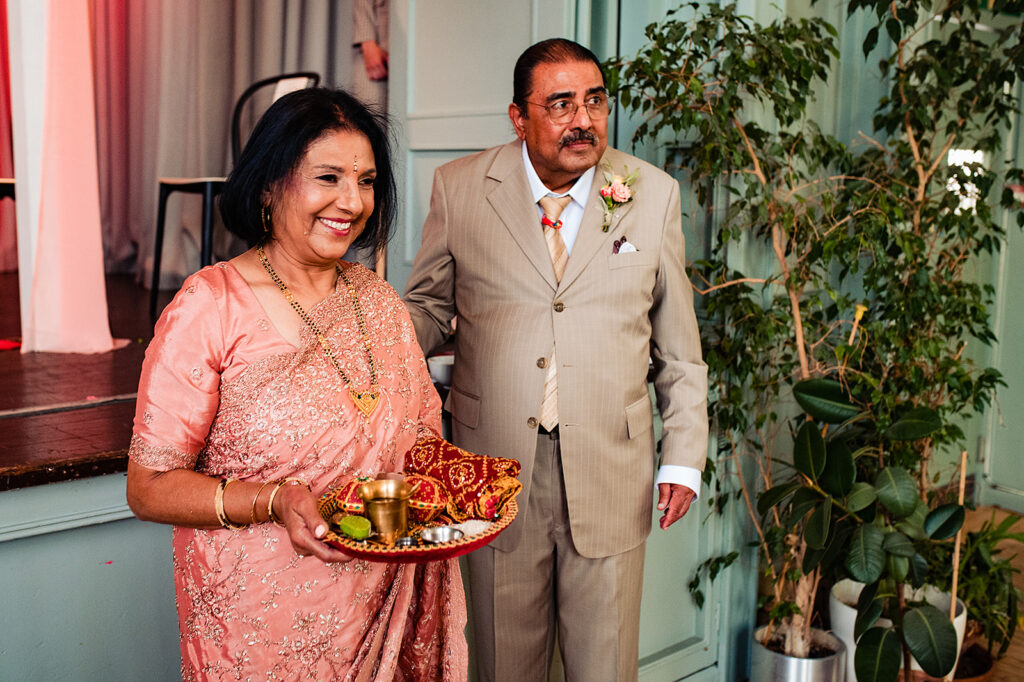 The mother of the bride and father of the bride at the start of the ceremony. The mother of the bride is wearing traditional Hindu attire of light pink and gold. Father of the bride is in a dusky cream linen suit.