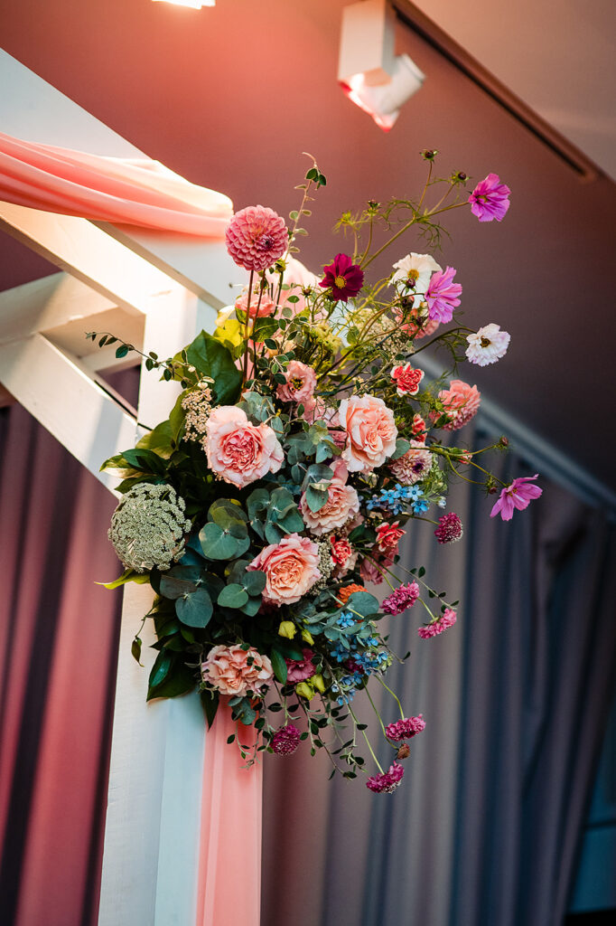 A big, bright floral piece attached to the ceremony arch. It's made up of pinks, reds, oranges, and green.