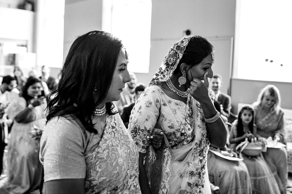 The bride wipes away a tear as she arrives at the end of the aisle at her hindu wedding ceremony